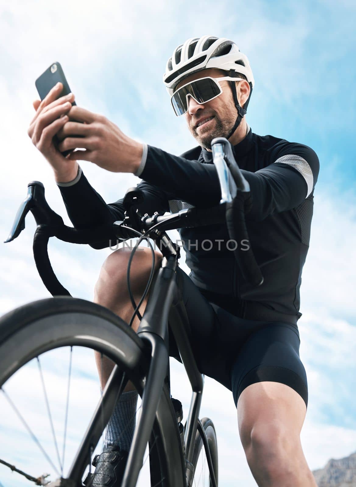 How far out am I. a handsome mature man sending a text while cycling outdoors. by YuriArcurs