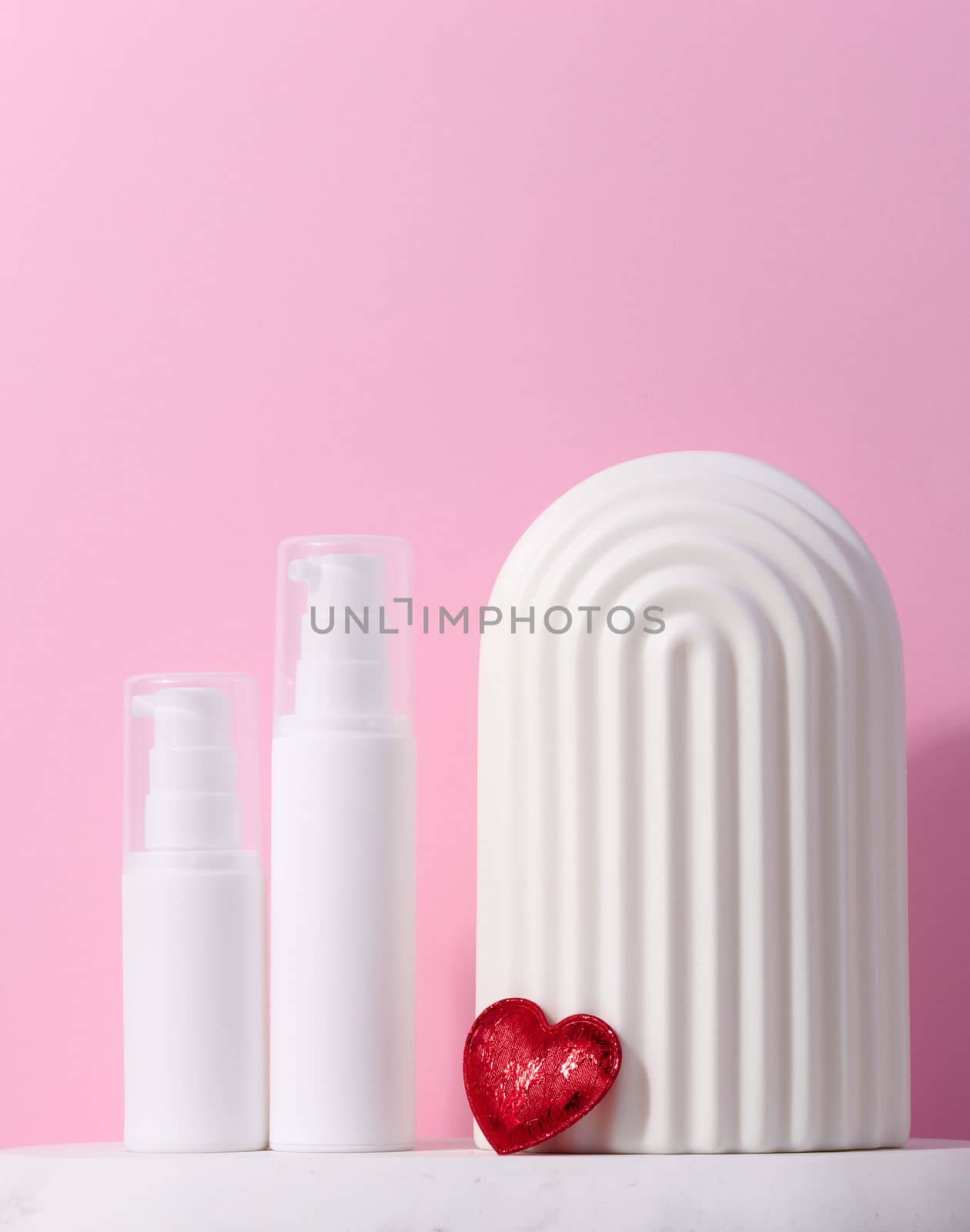 A white plastic tub with a dispenser stands on a marble stand and a ceramic decorative arch, cosmetic container