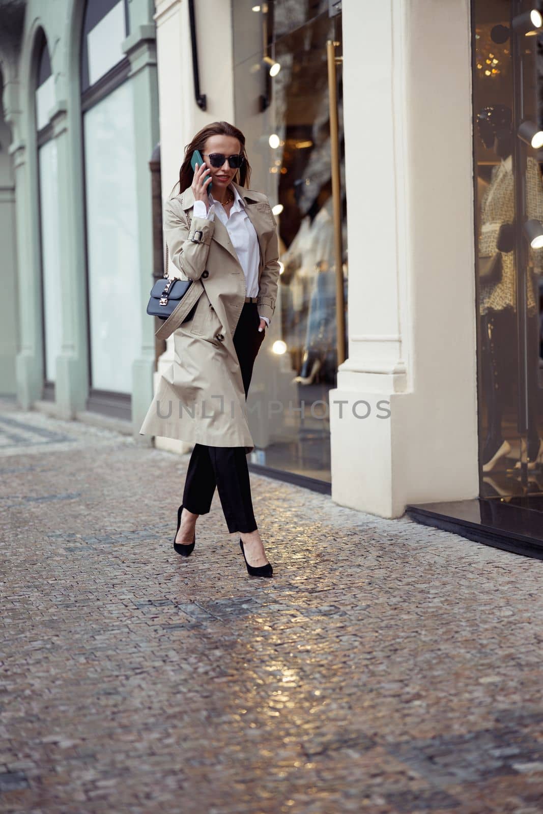 Stylish european woman in sunglasses is talking phone on city street background by Yaroslav_astakhov