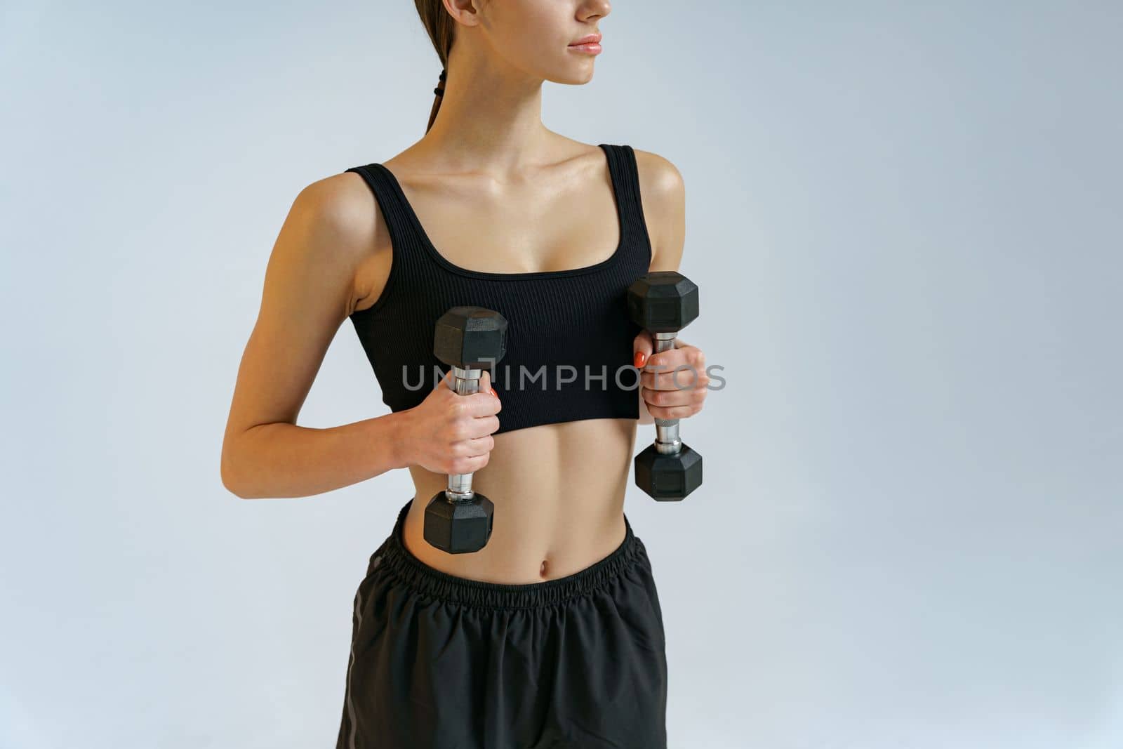 Close up of fitness woman doing exercises with dumbbells on studio background and looking at camera by Yaroslav_astakhov