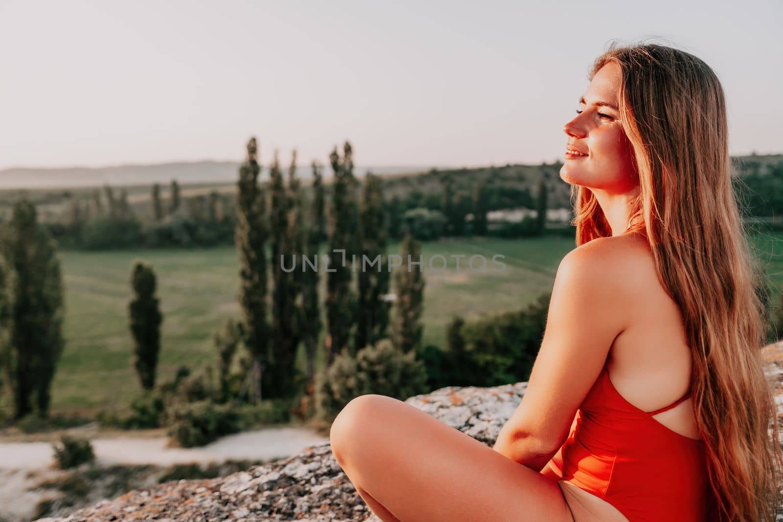 Well looking middle aged woman with long hair, fitness instructor in leggings and tops doing stretching and pilates on the rock near forest. Female fitness yoga routine concept. Healthy lifestyle by panophotograph