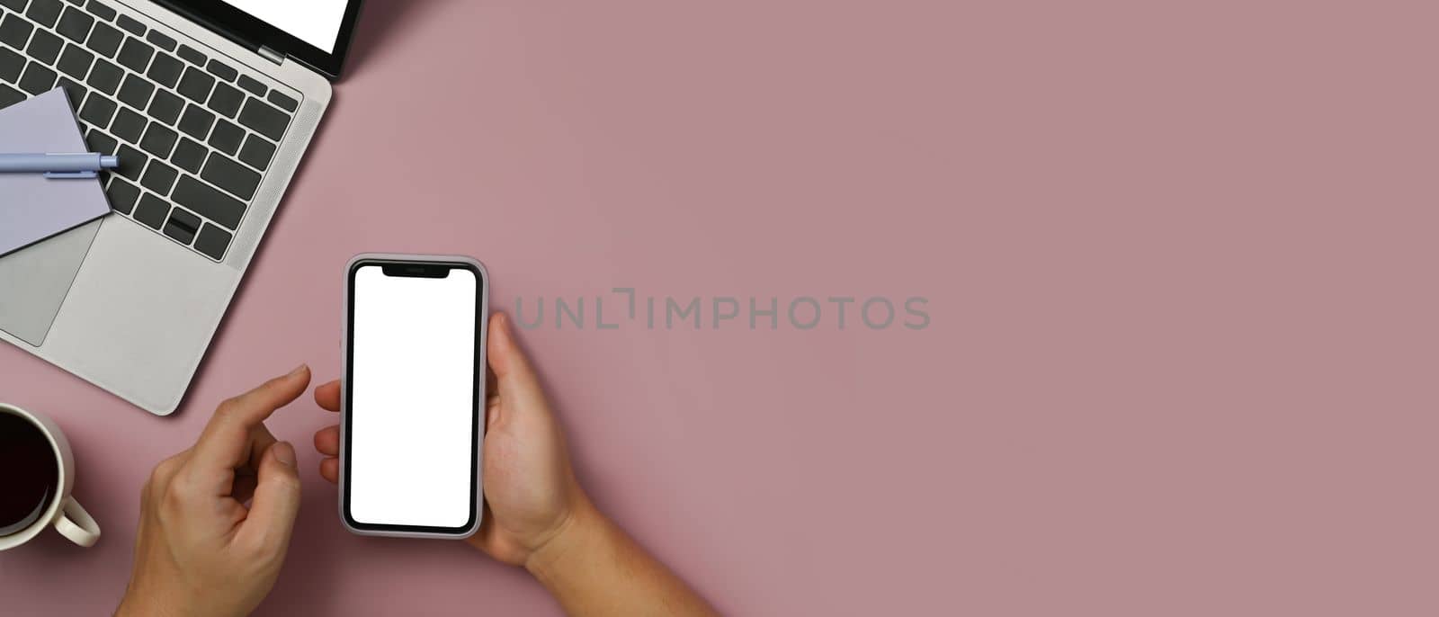 Woman hands holding mock up smart phone with blank screen over pink background. Top view with copy space for your text by prathanchorruangsak
