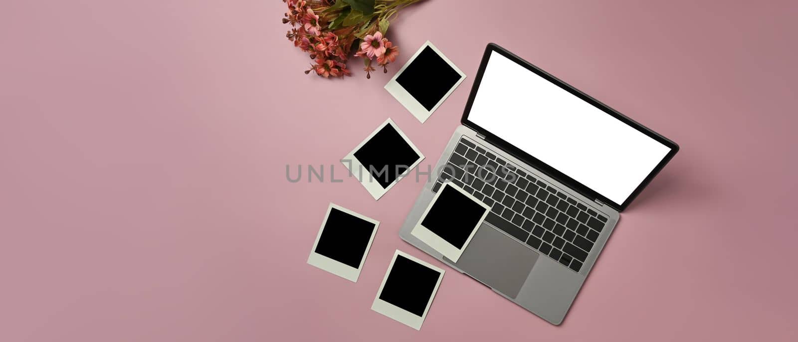 Laptop computer with white screen, blank photo frames and beautiful blooming flower bouquet on pink background by prathanchorruangsak
