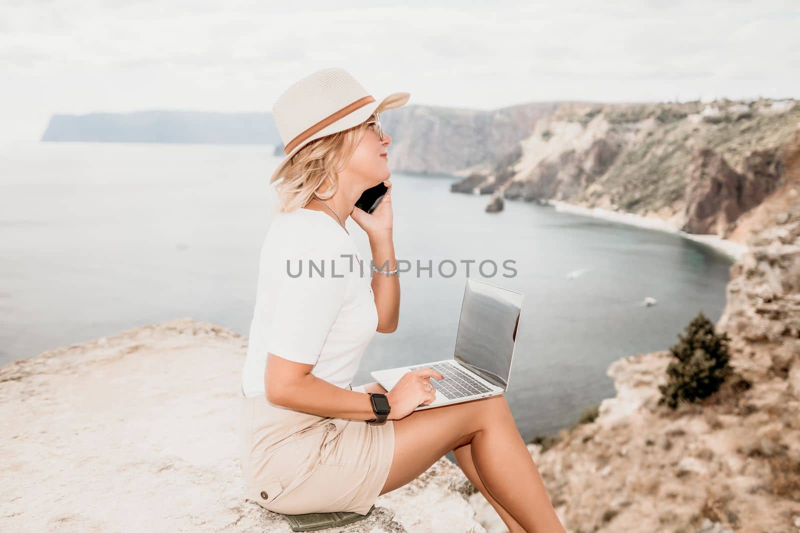 Digital nomad, Business woman working on laptop by the sea. Pretty lady typing on computer by the sea at sunset, makes a business transaction online from a distance. Freelance remote work on vacation