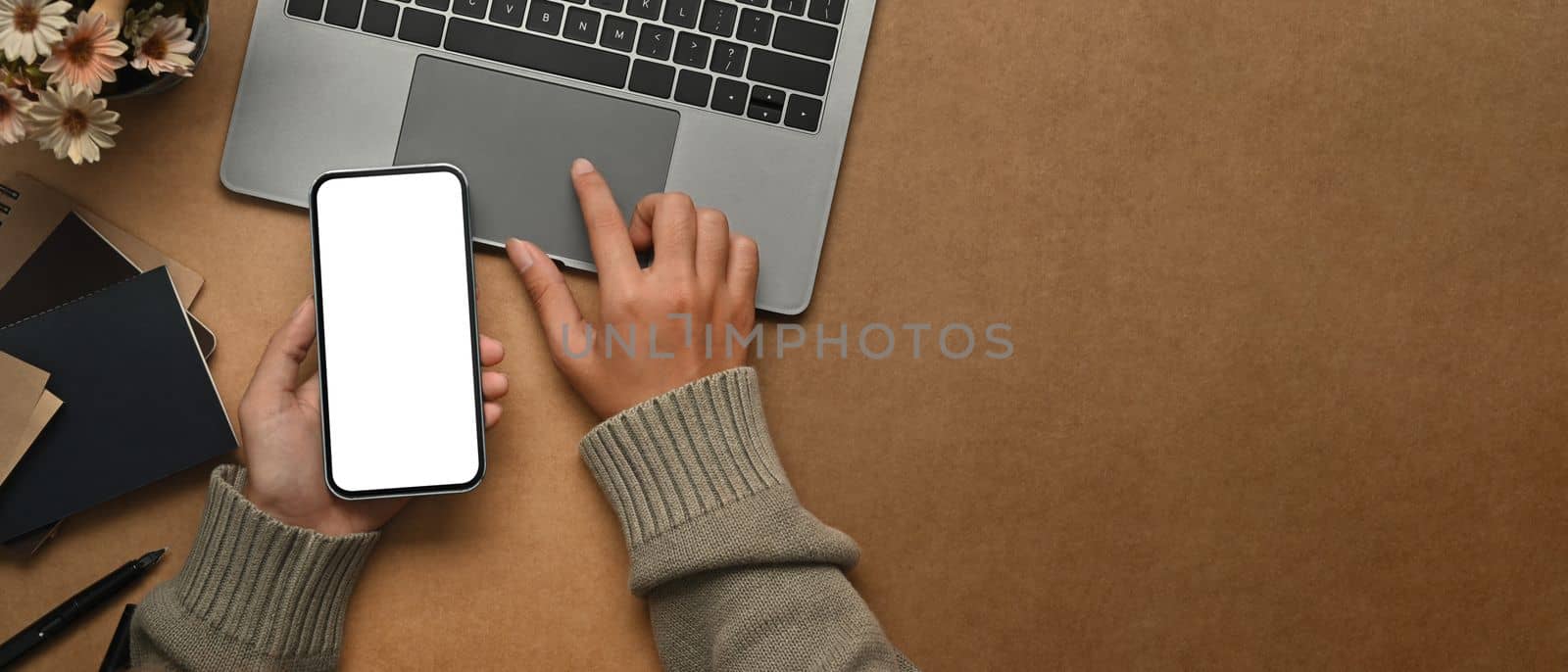 From above view of woman hand holding mobile phone with blank screen and typing on laptop computer.
