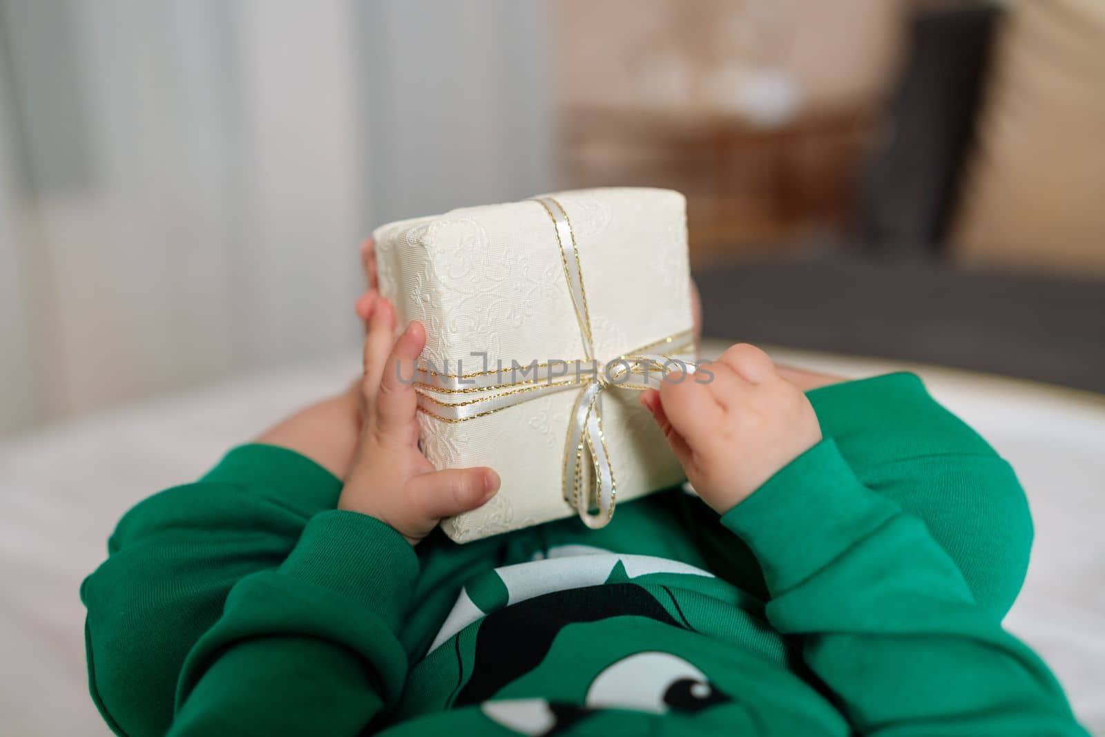 Kid gift. A little boy in a green suit holds a gift box with his feet and hands in bed