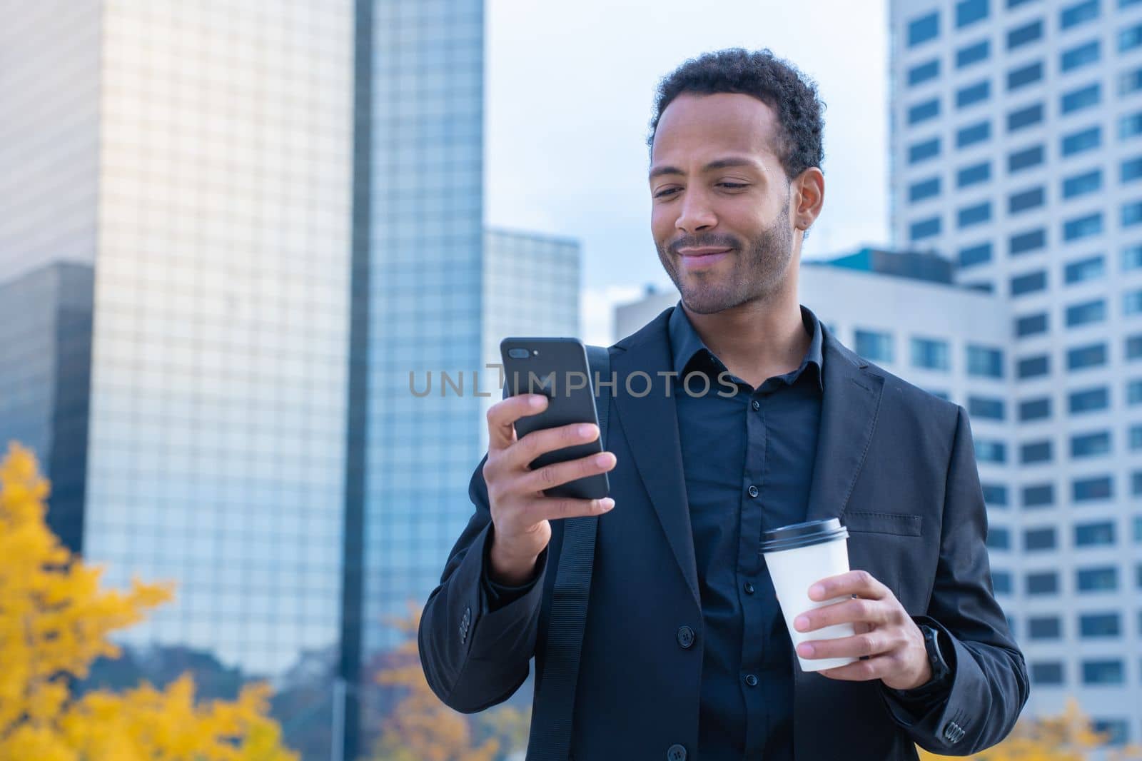 Successful black businessman in suit smiling with smart phone and coffee cup in financial district by PaulCarr