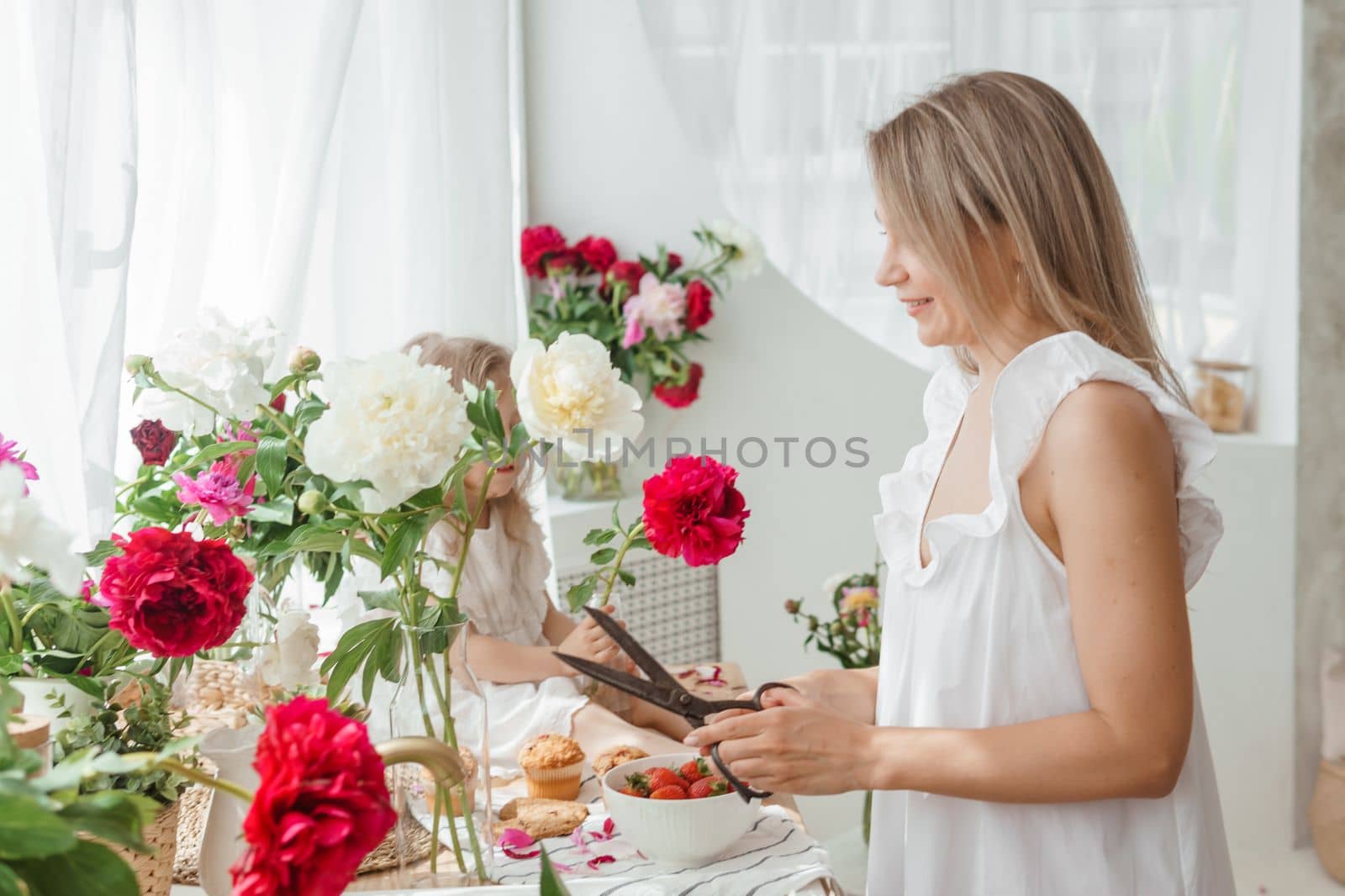 A little blonde girl with her mom on a kitchen countertop decorated with peonies. The concept of the relationship between mother and daughter. Spring atmosphere.