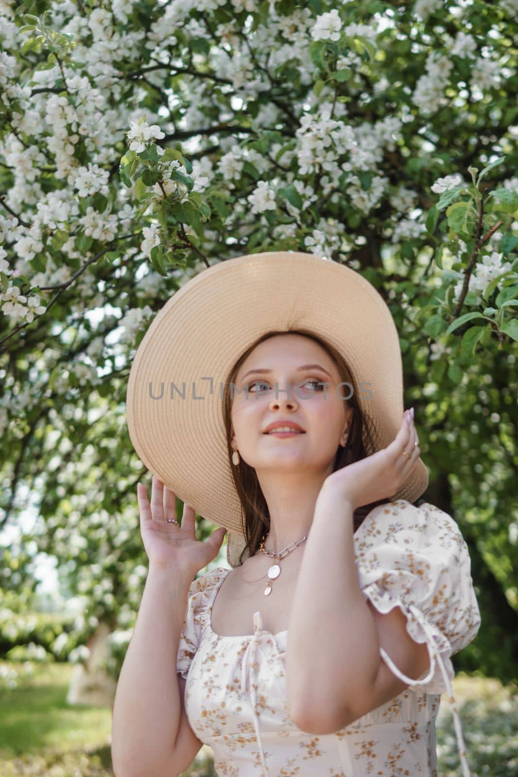 An attractive long-haired woman walks in the spring in the park of blooming apple trees. Spring portrait of a woman