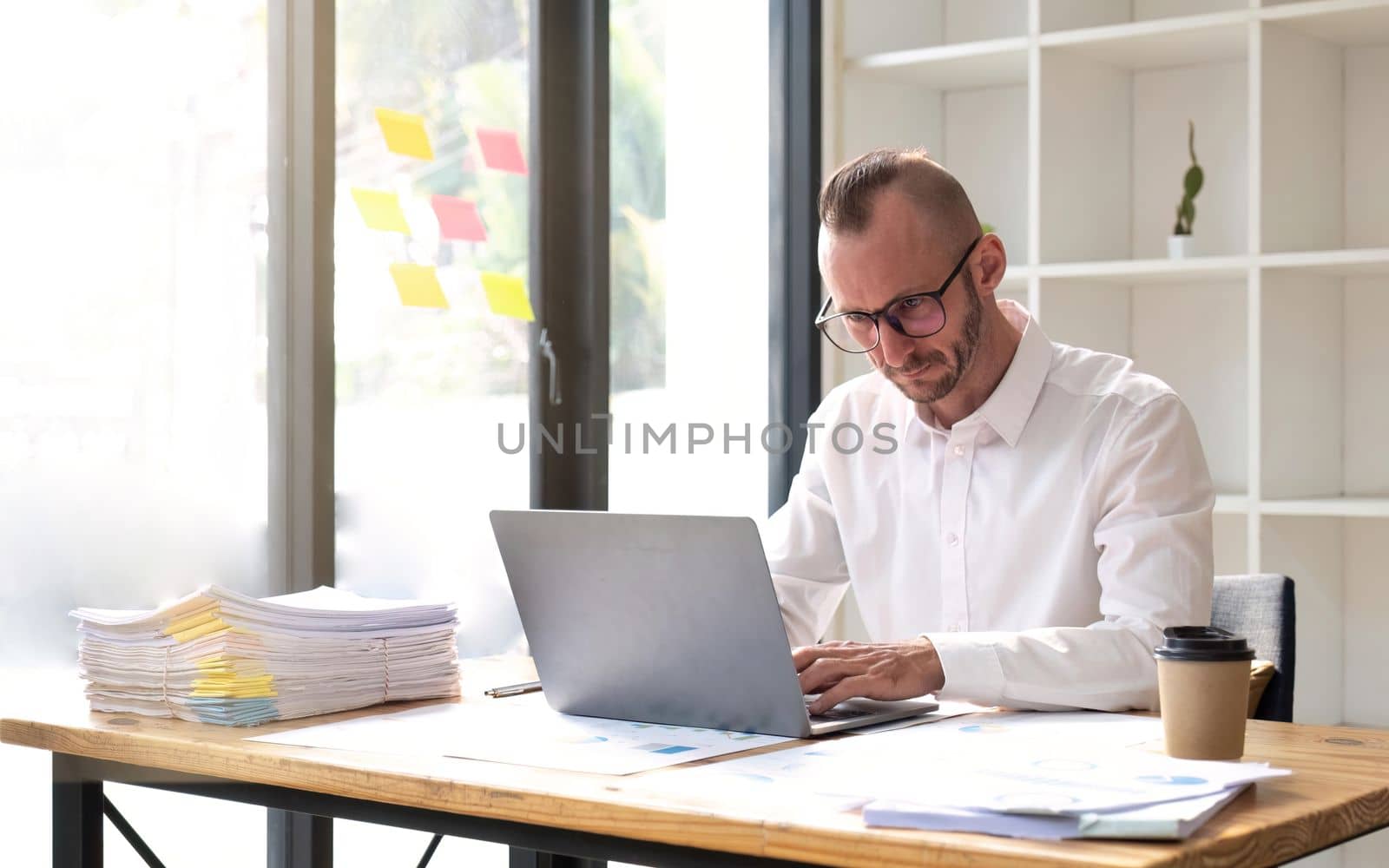 Young business man working at office with laptop and papers on desk.