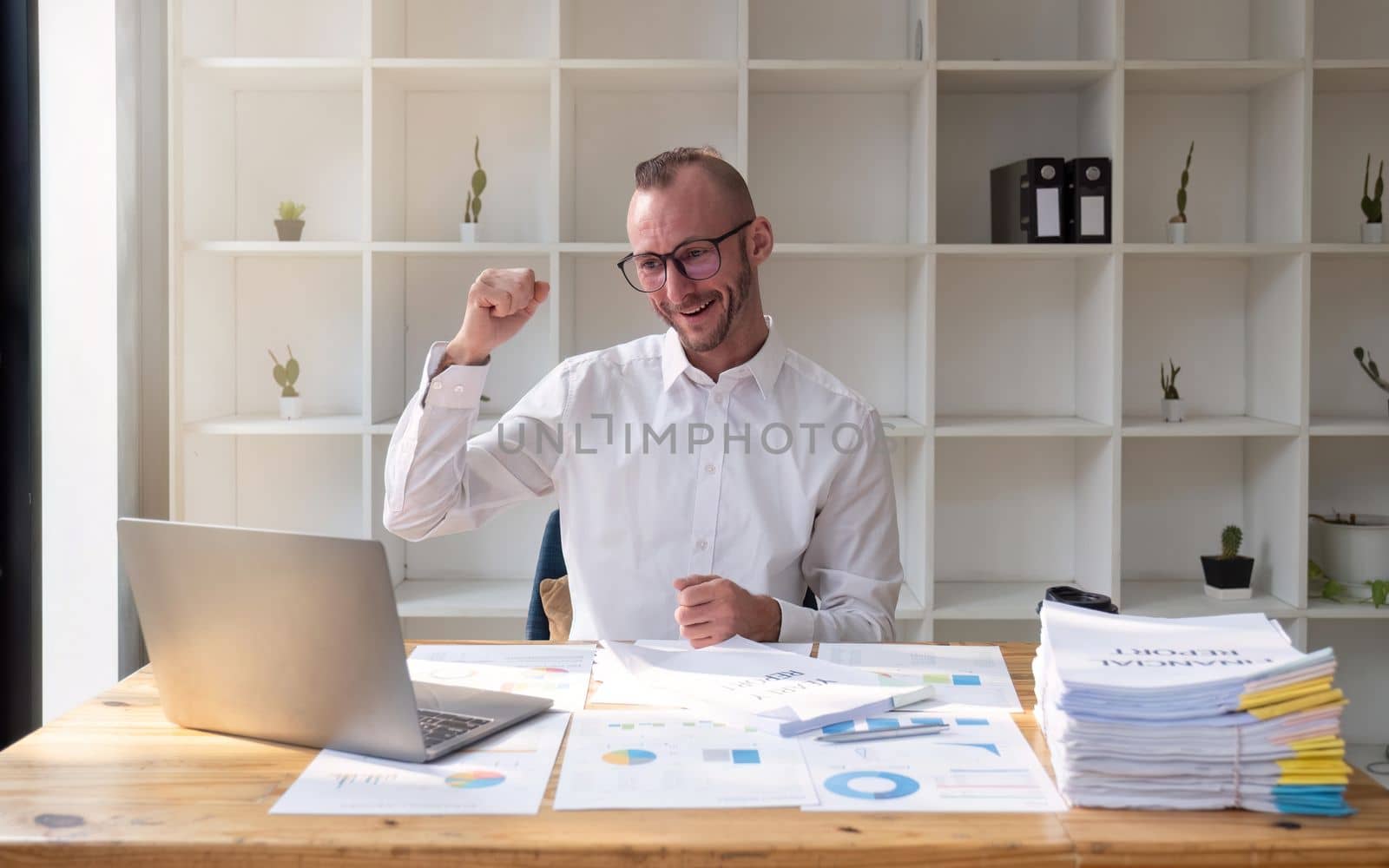 Cheerful young businessman celebrating success handsome in and raising hands up at office.