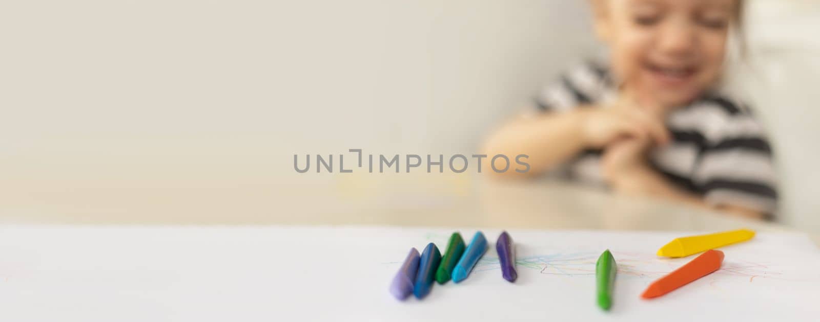 Selective focus on colorful crayons. Happy caucasian baby girl sitting at the table at home. Banner for early development. Copy space. by Ri6ka