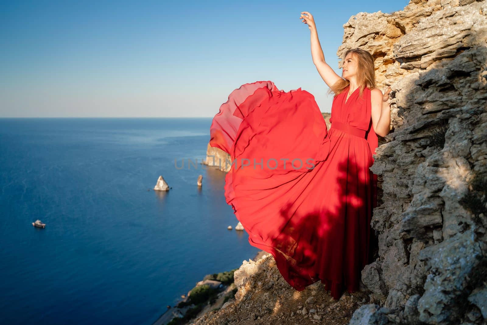 A woman in a red flying dress fluttering in the wind, against the backdrop of the sea. by Matiunina