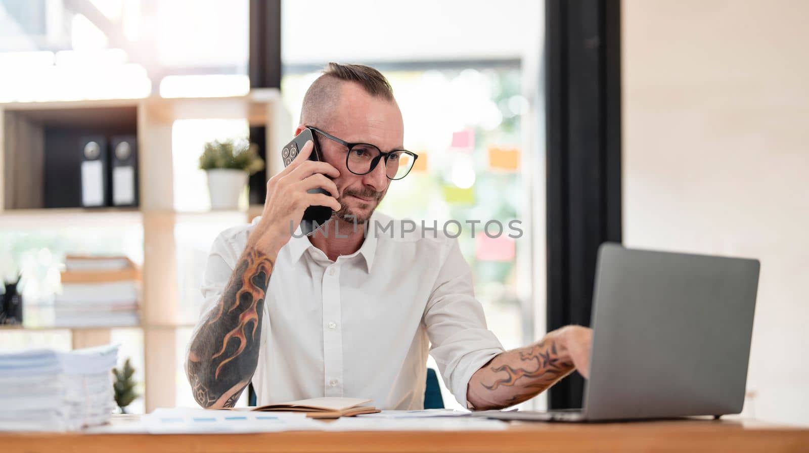 Handsome mature businessman is talking on the mobile phone and smiling while working in office..