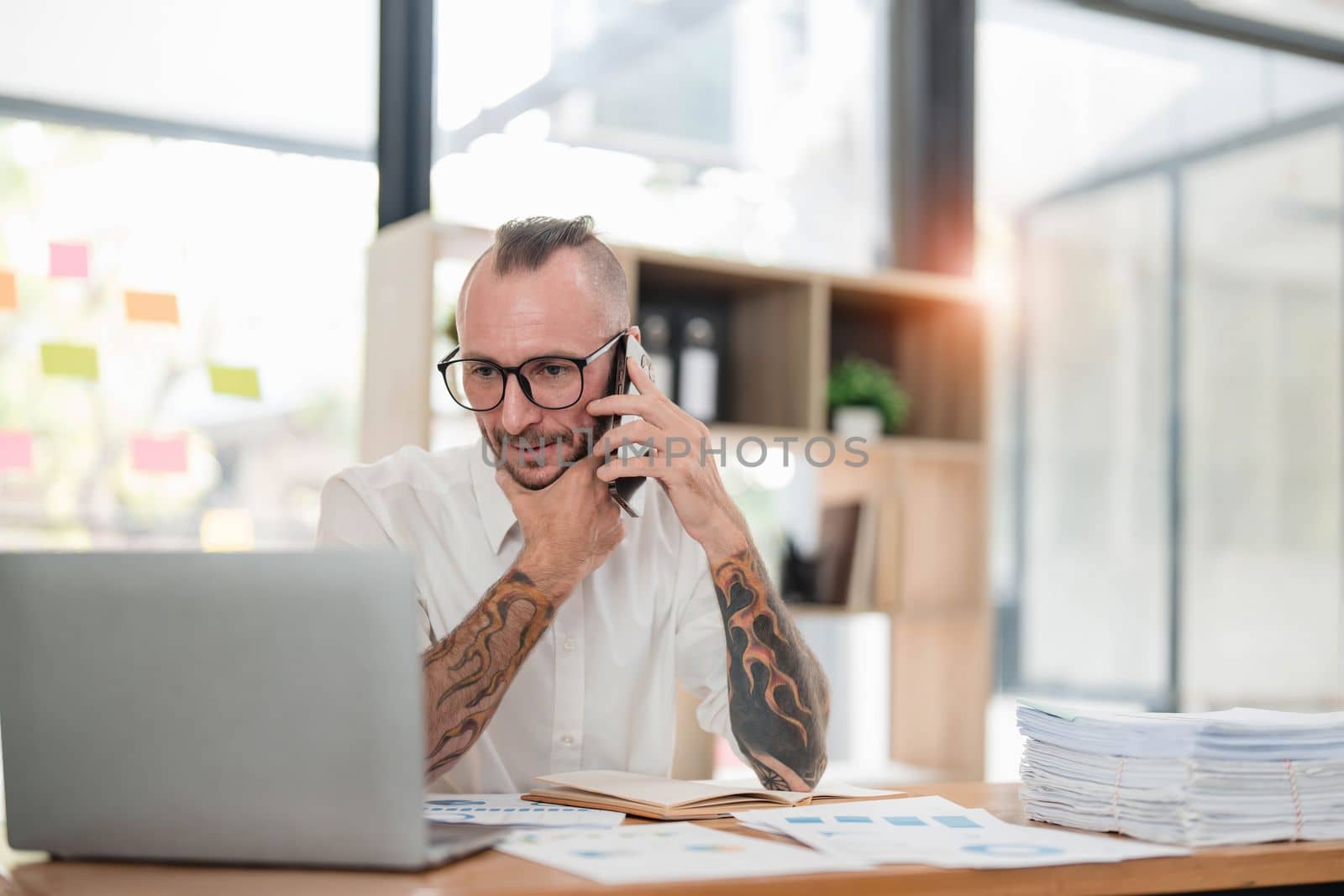 Handsome mature businessman is talking on the mobile phone and smiling while working in office by wichayada