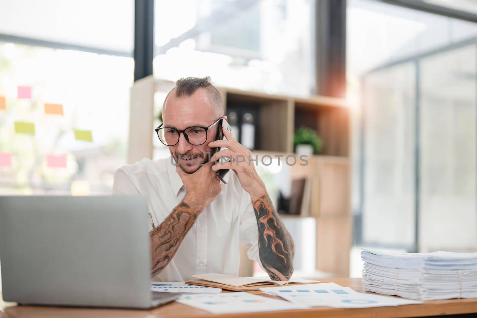 Handsome mature businessman is talking on the mobile phone and smiling while working in office..