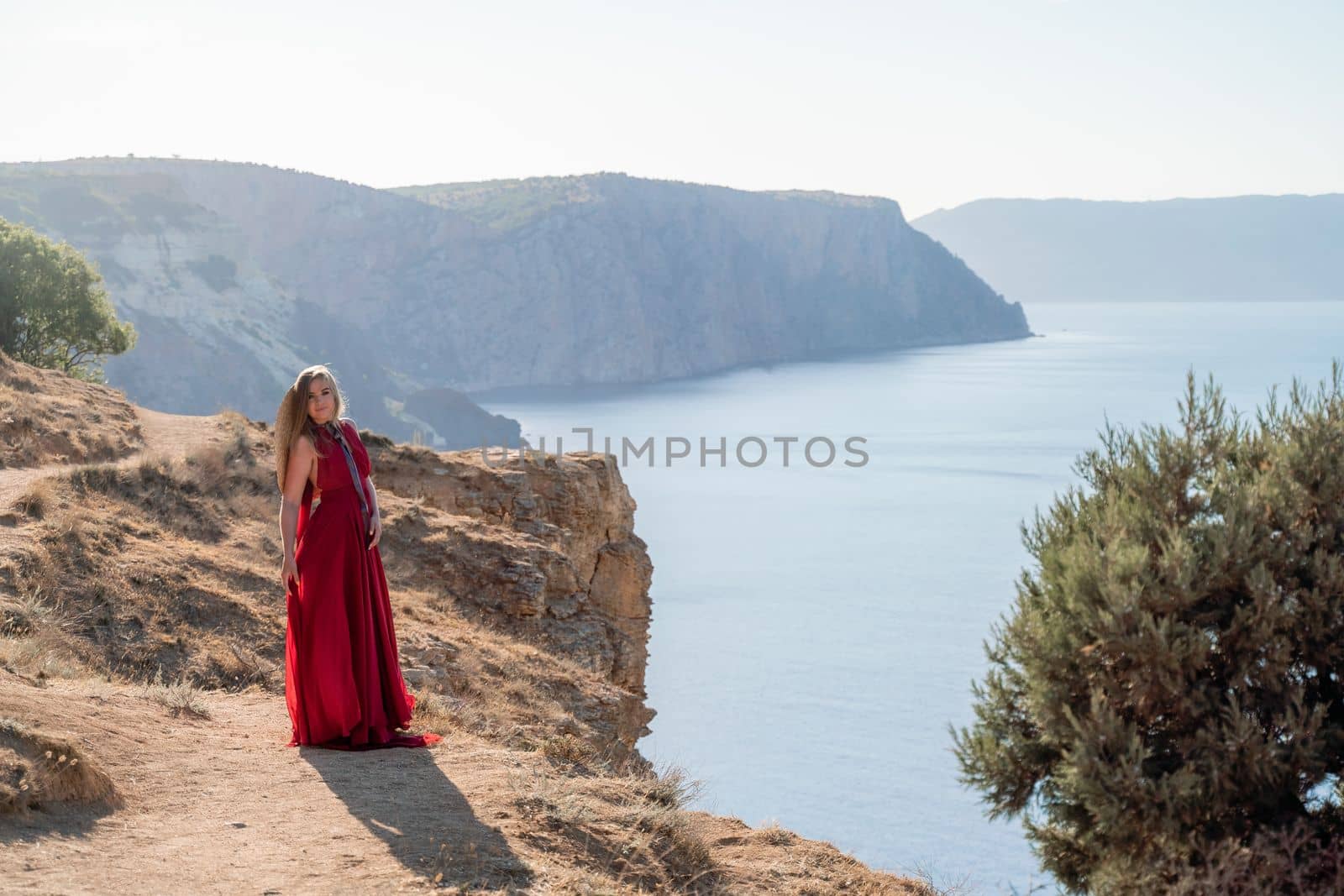 A woman in a red flying dress fluttering in the wind, against the backdrop of the sea. by Matiunina