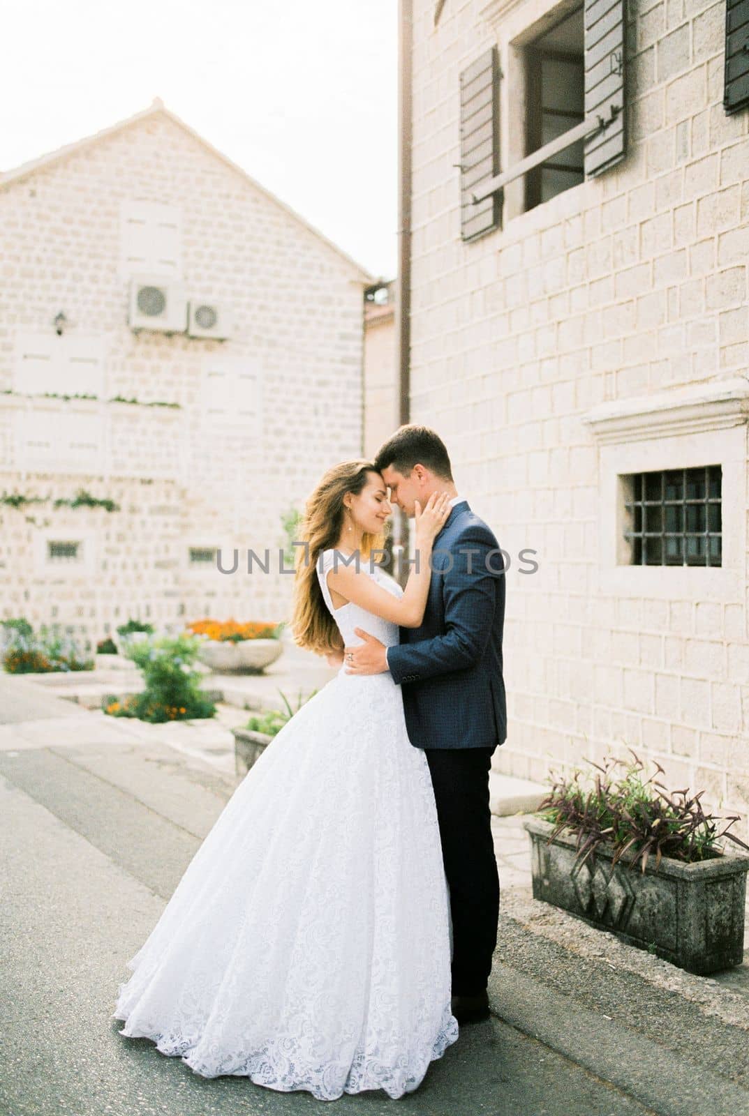 Groom hugs bride near the old stone house on the street. High quality photo