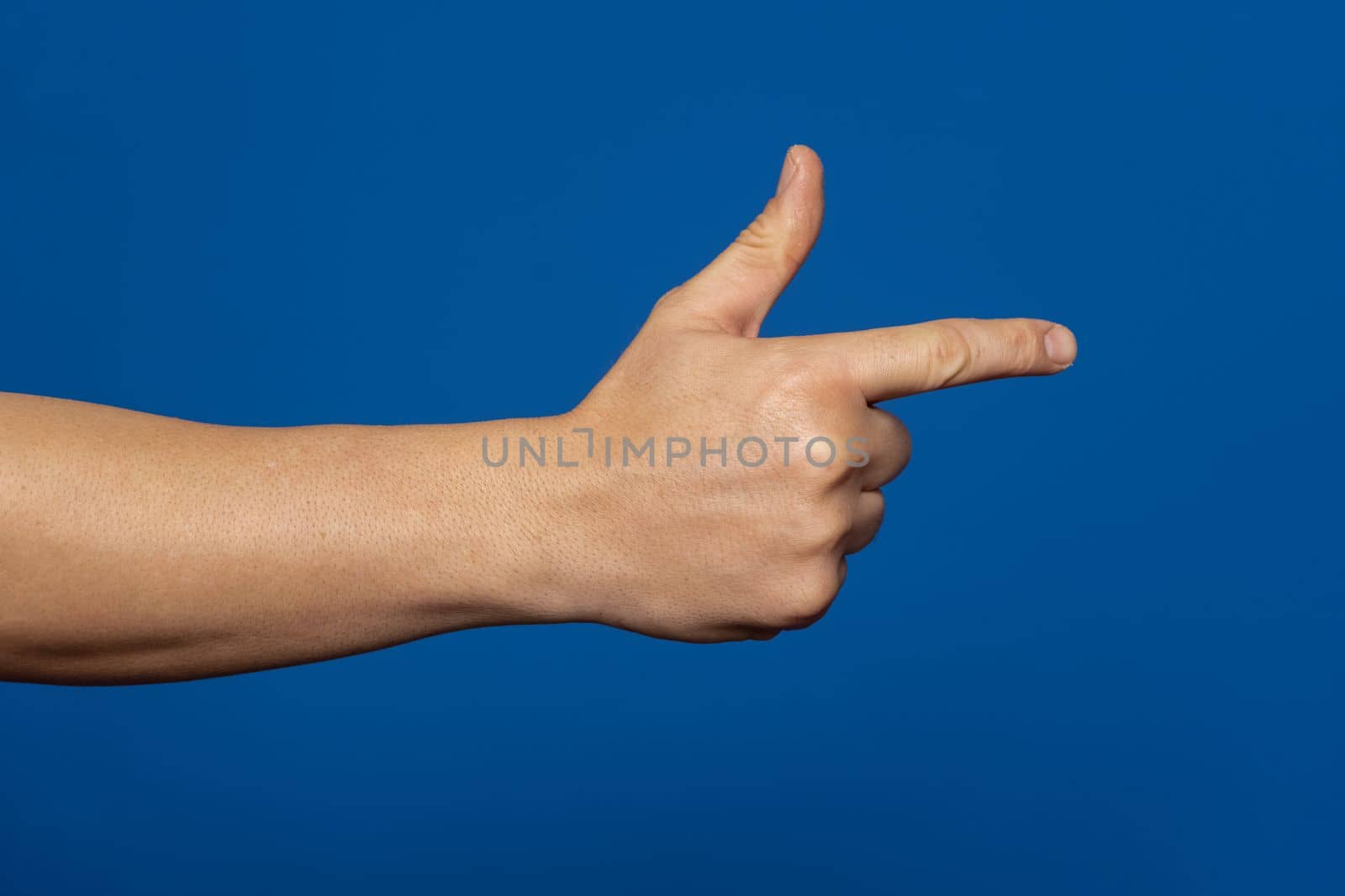 Man's hand making shooting, gesture. Hand gun gesture on isolated blue background. Man's hand pointing a finger.