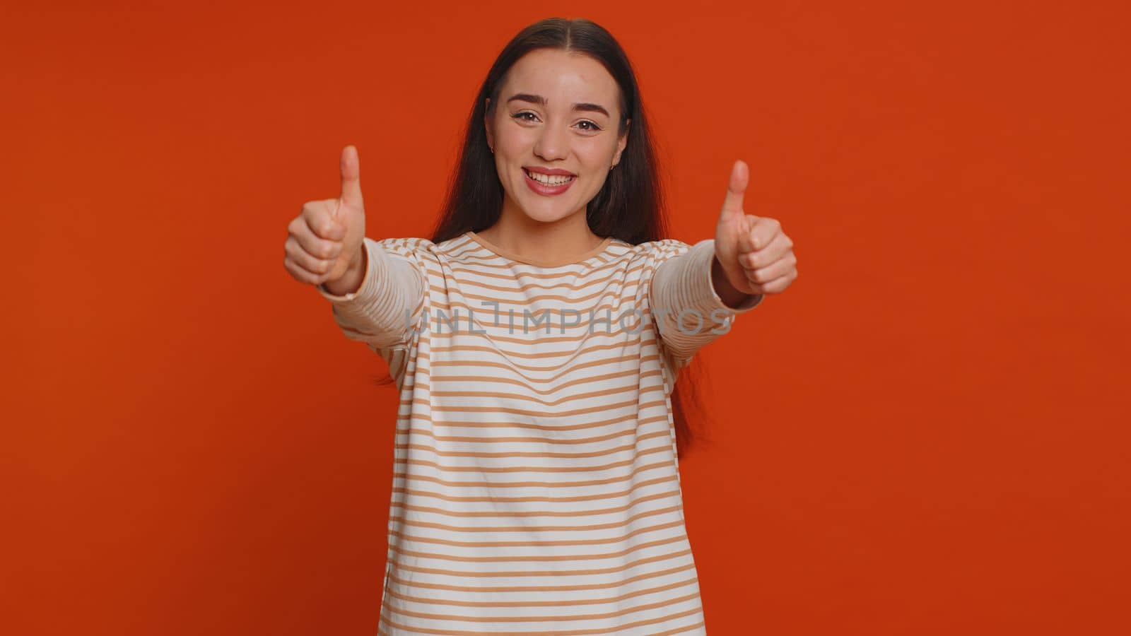 Like. Hipster one pretty woman in pullover raises thumbs up agrees with something or gives positive reply recommends advertisement likes good. Young girl isolated alone on red studio background