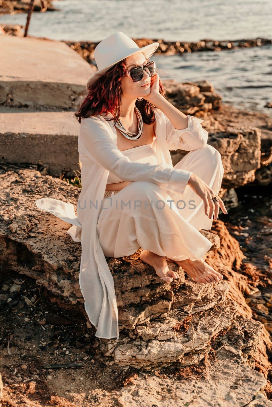 A woman in a white pantsuit and hat is standing on the beach enjoying the sea. Happy summer holidays.