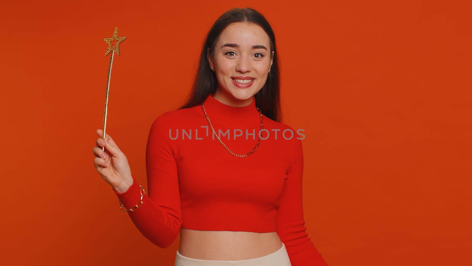 Magician witch woman gesturing with magic wand fairy stick, making wish come true, casting magician spell, advertising holidays sale discount. Young pretty girl isolated on red studio background
