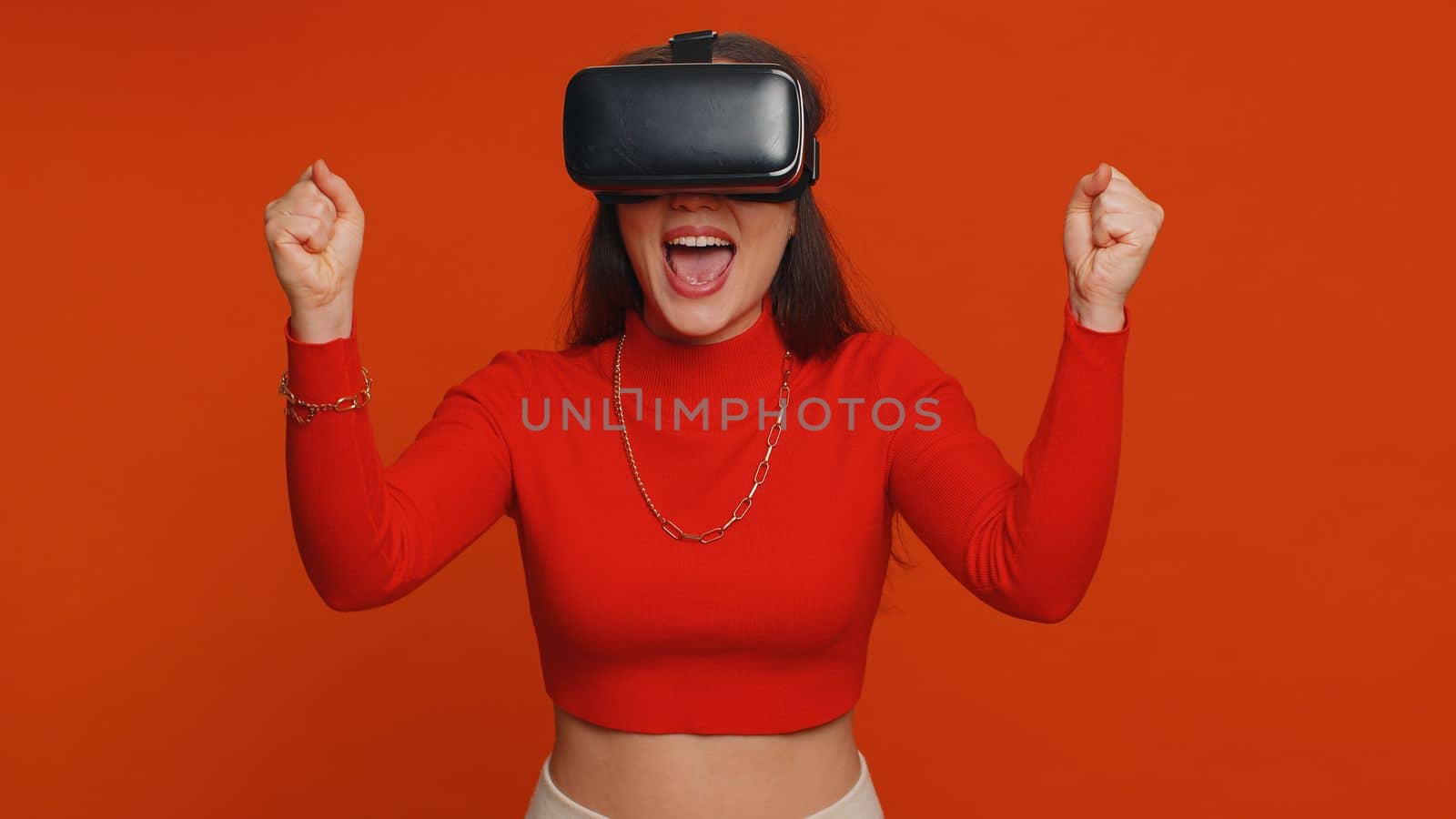 Lovely woman using headset helmet to play simulation game app online. Watching virtual reality 3D 360 video content. One girl in VR goggles isolated on studio red background. Futuristic technology