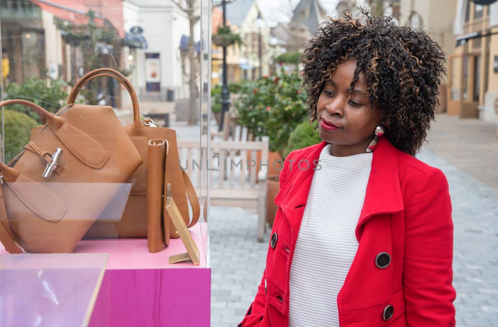 Happy confident curvy african american woman walks along a shopping street and looks at stylish bags in a shop window, High quality photo