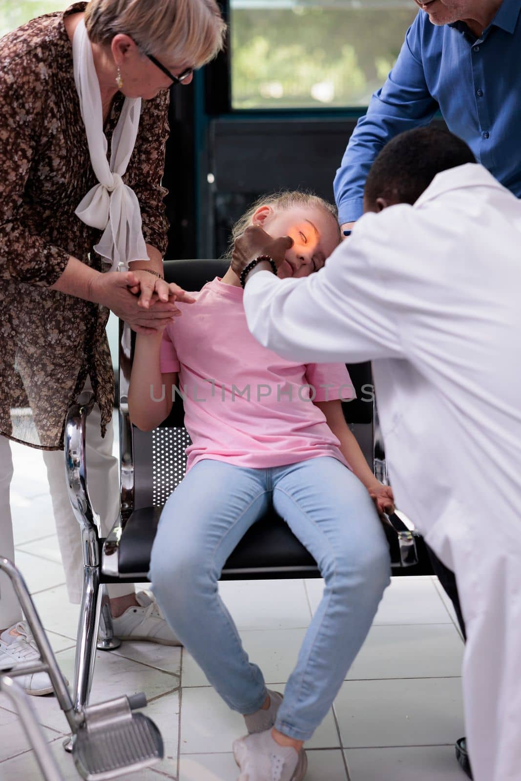 Practitioner doctor shining light into little girl patient eye while testing pupil reflexes during checkup visit by DCStudio