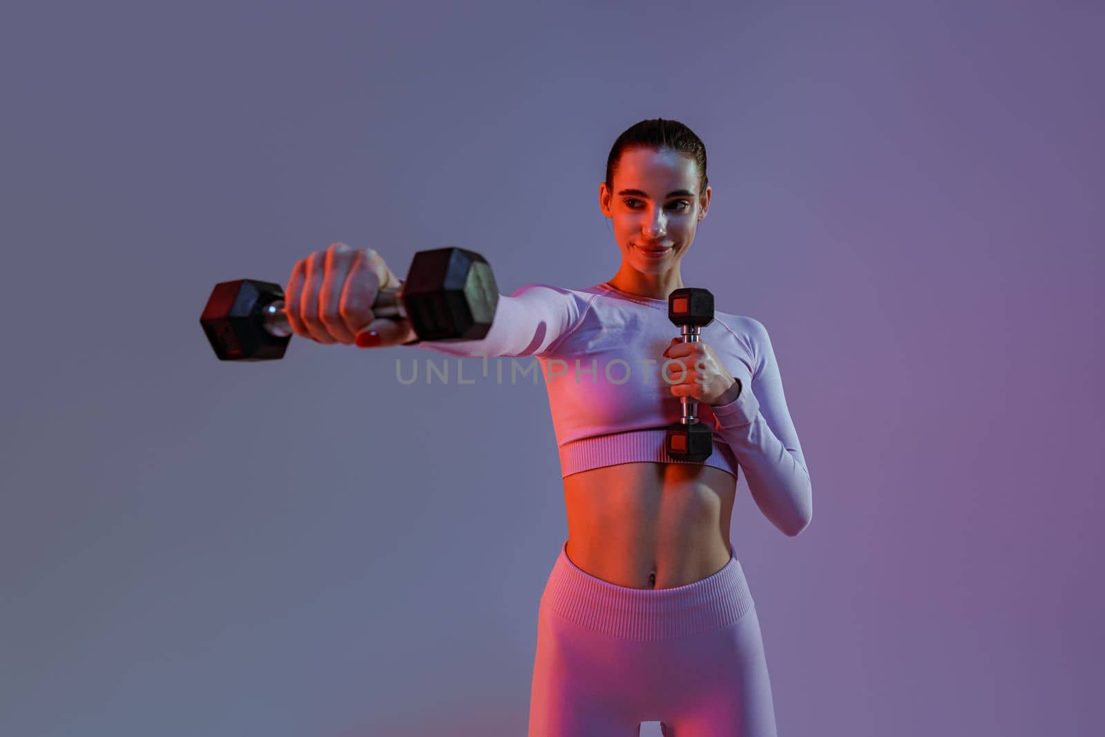 Pretty fitness woman doing exercises with dumbbells on studio background. Strength and motivation by Yaroslav_astakhov