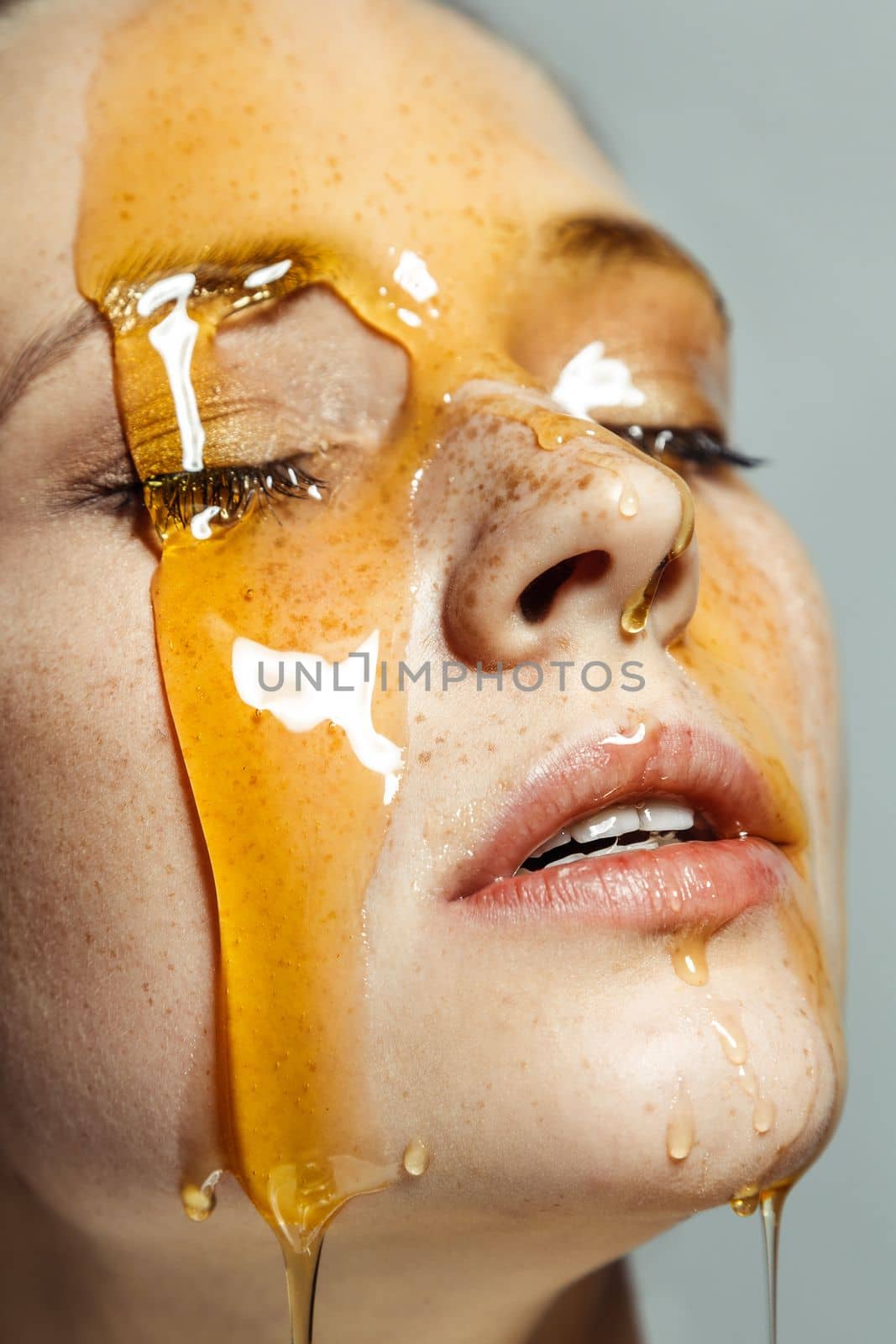 Closeup profile portrait of cute adorable young woman with freckles and honey on face, standing with closed eyes, being satisfied of cosmetic procedures. Indoor studio shot isolated on gray background