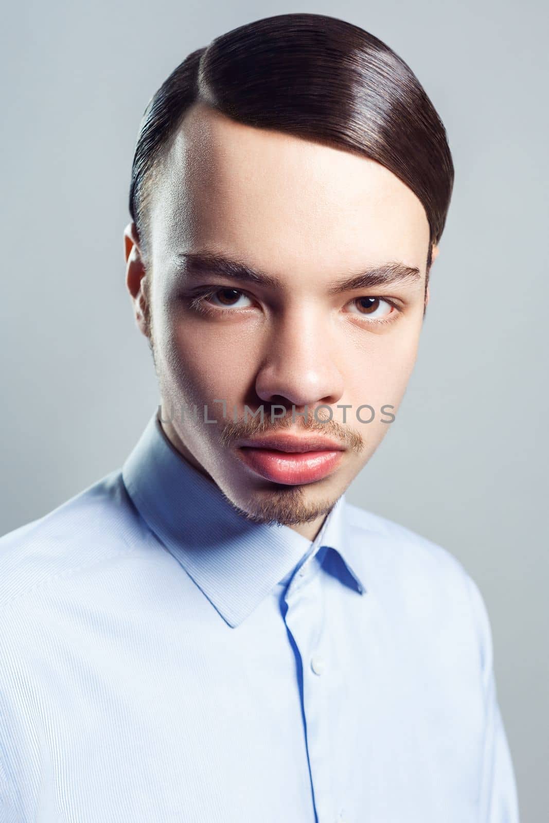 Portrait of young attractive handsome serious man with mustache with retro classic hairstyle, looking at camera, wearing blue shirt. Indoor studio shot isolated on gray background.