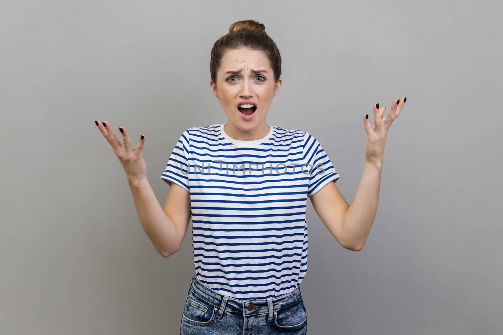 What's the problem. Portrait of irritated indignant woman wearing T-shirt raising hands in anger and shouting why how, what do you want, quarreling. Indoor studio shot isolated on gray background.