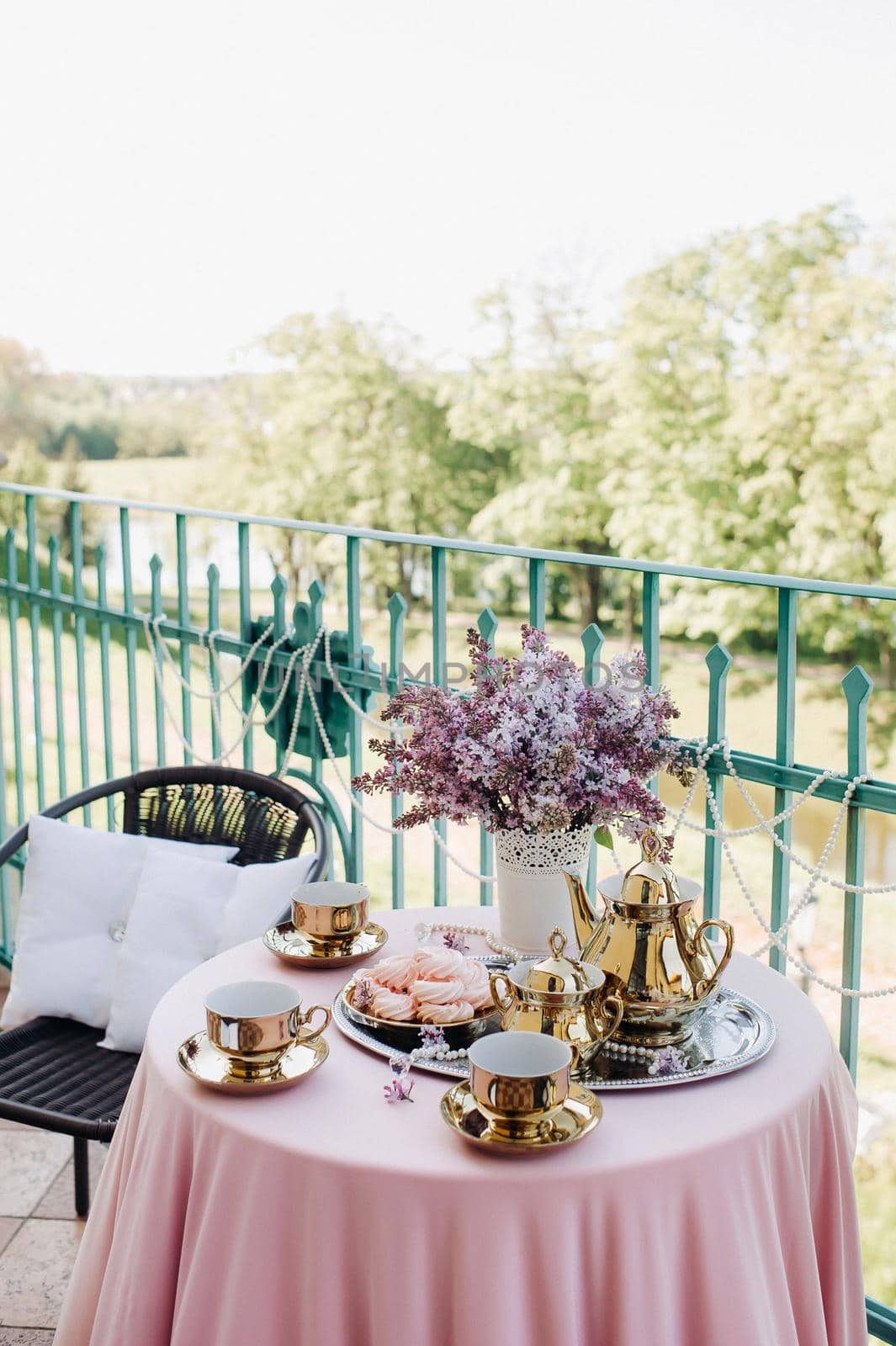 Delicate morning tea table setting with lilac flowers in Nesvizh castle, antique spoons and dishes on the table with a pink tablecloth.