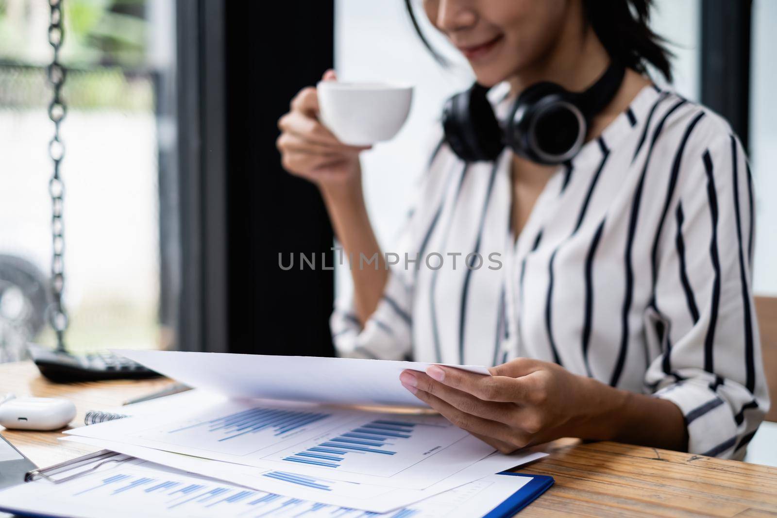 Businesswoman working to analyze technical price graph and indicator holding cup of coffee at morning. by itchaznong