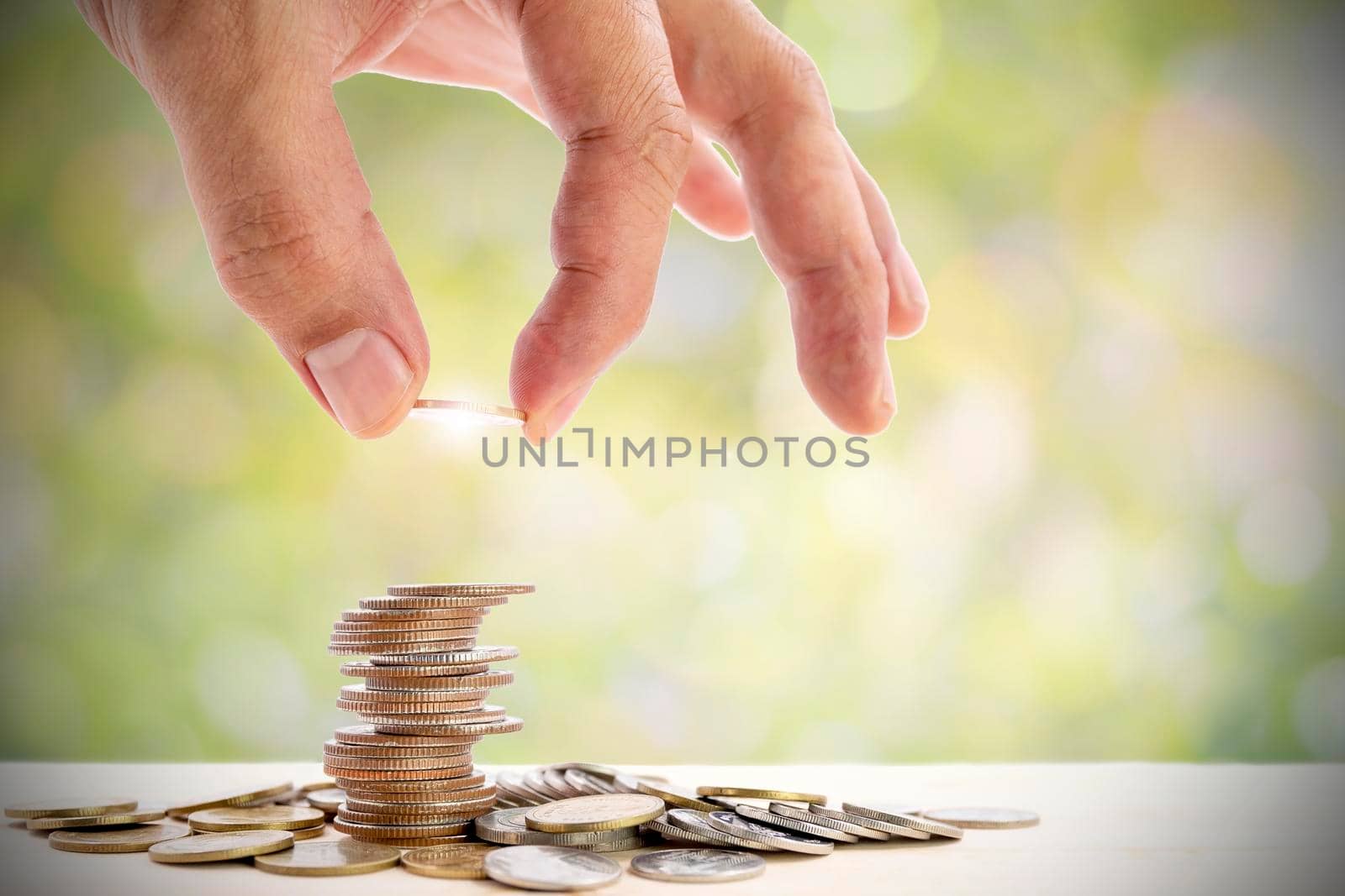 Human hand placing a coin on a pile of coins, use for for business and financial growth concepts.