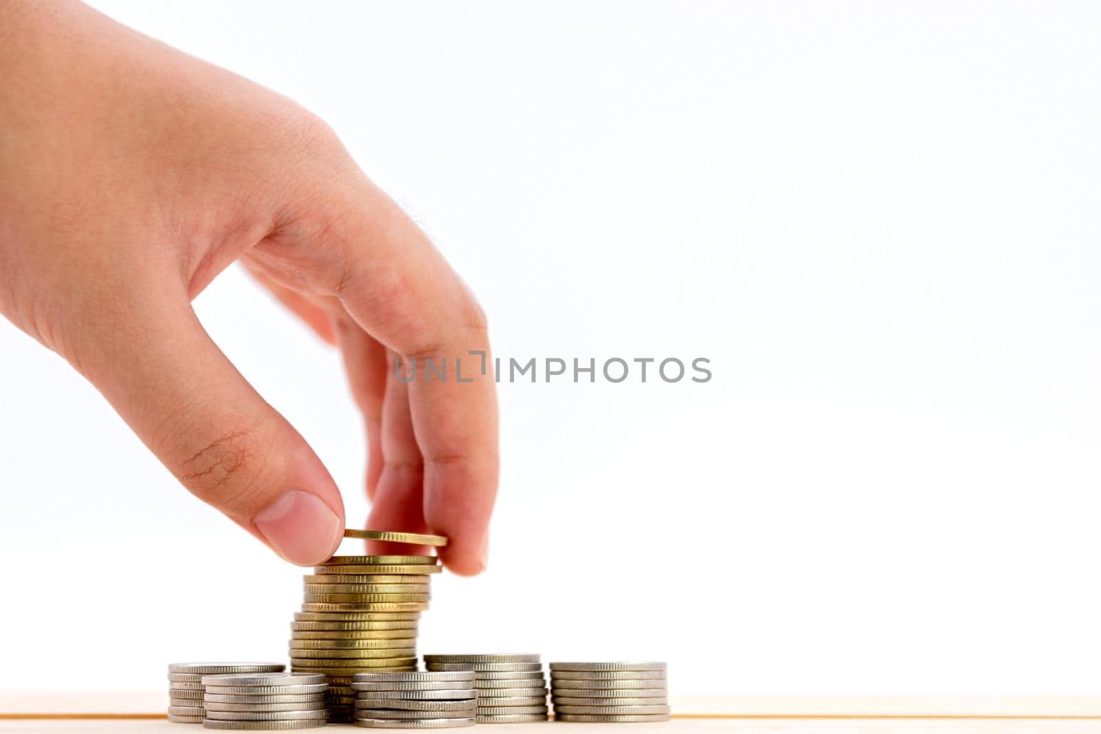 Closeup of human hand putting a coin on a pile of coins over white background, use for business and finance concepts.