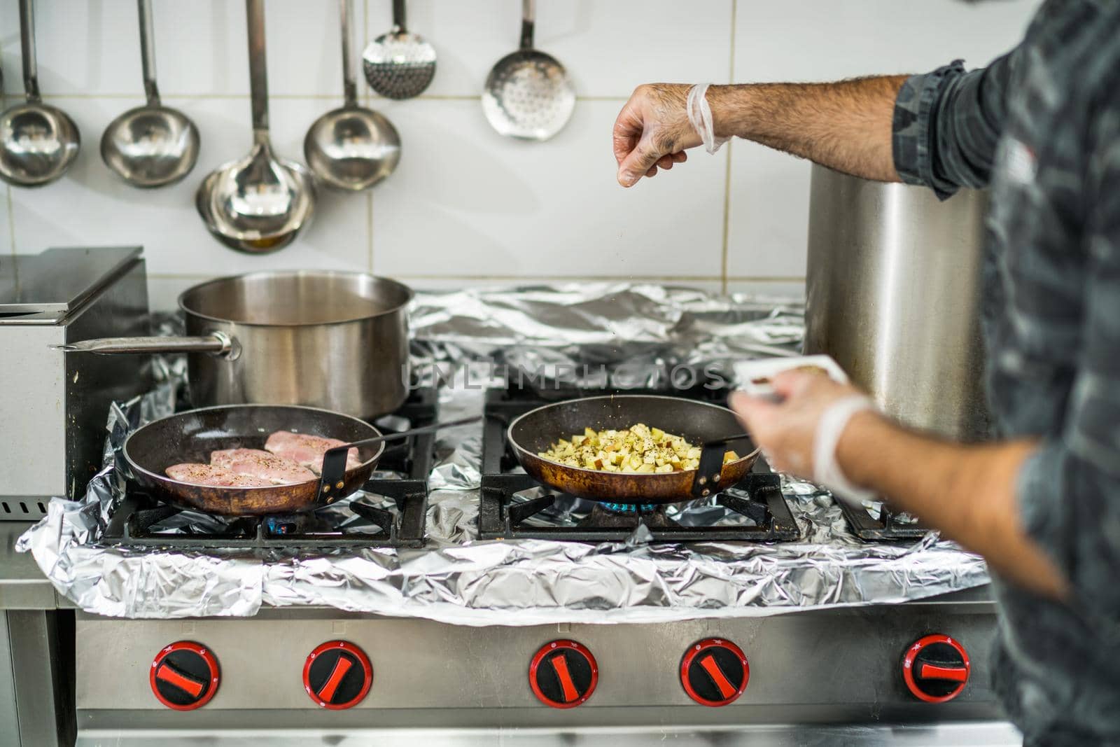 Professional cook is preparing meal in restaurant's kitchen. He is inserting spices in meal during cooking.