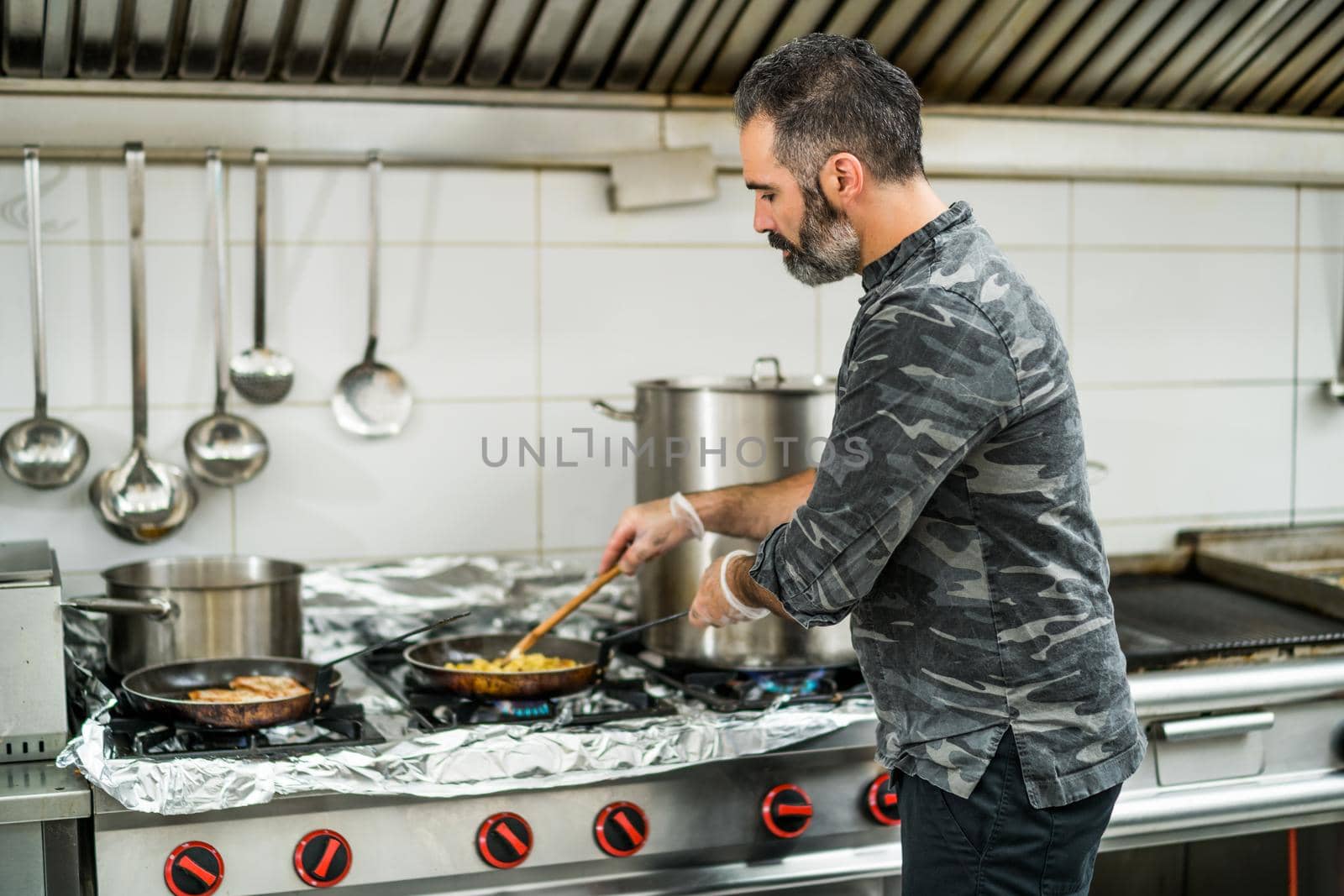 Professional cook is preparing meal in restaurant's kitchen. He is mixing food during frying.\