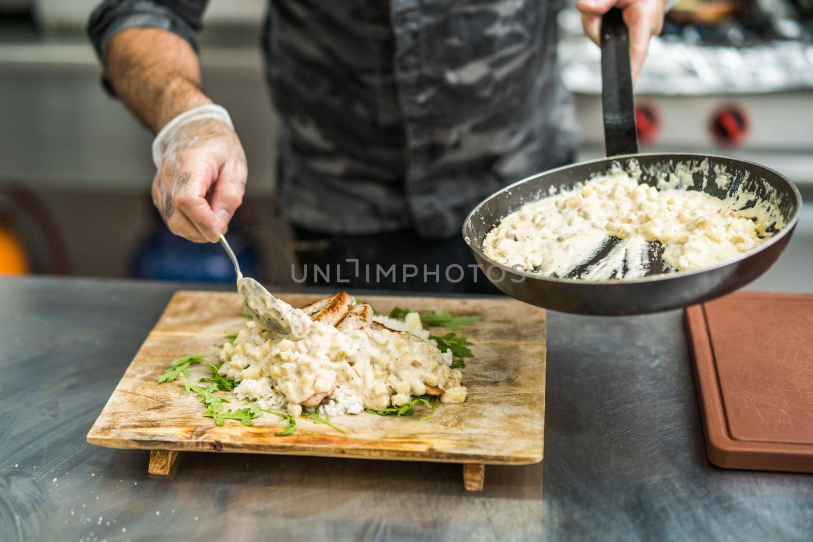 Professional cook is serving meal in restaurant's kitchen.