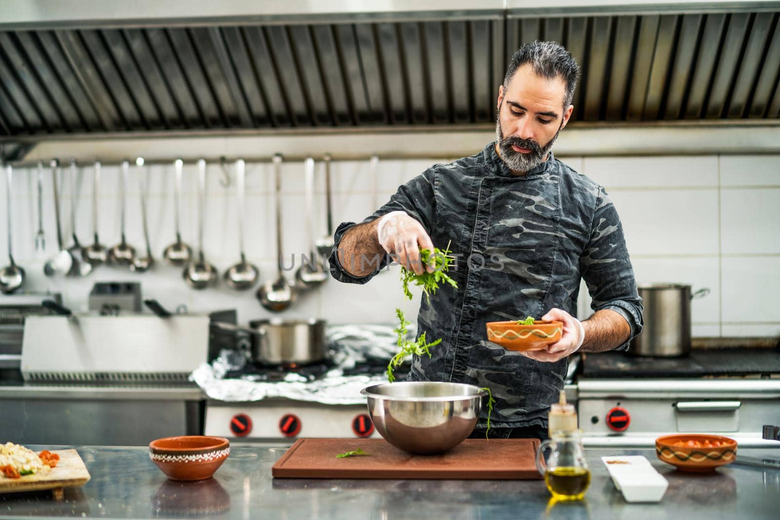 Professional cook is preparing meal in restaurant's kitchen. He is making salad.