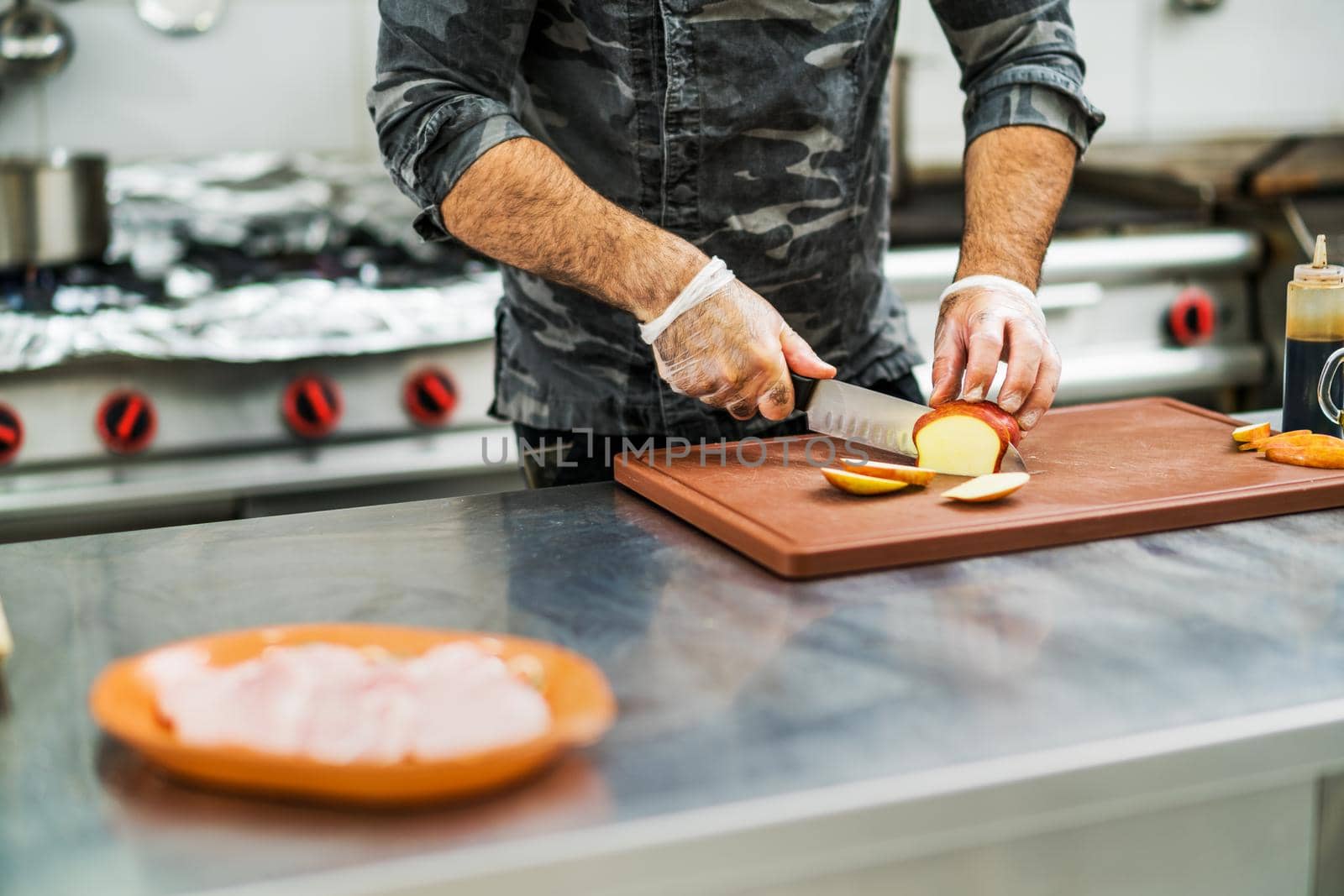 Professional cook is preparing meal in restaurant's kitchen. He is cutting apples.