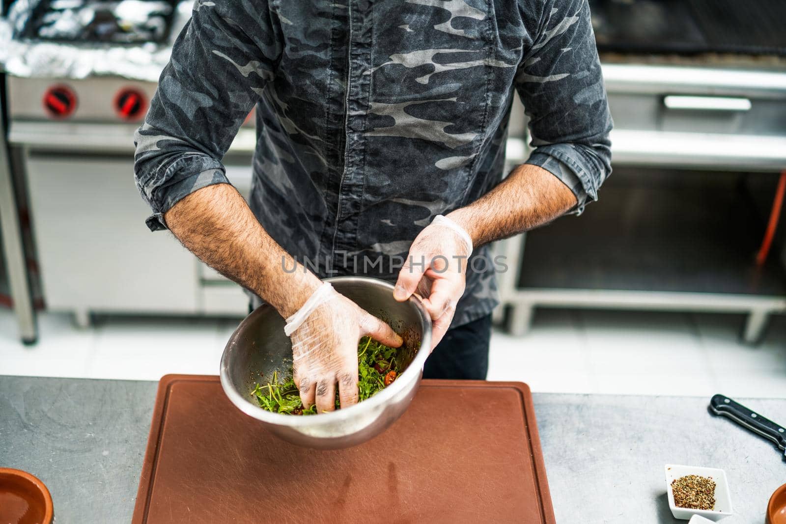 Professional cook is preparing meal in restaurant's kitchen. He is making salad.