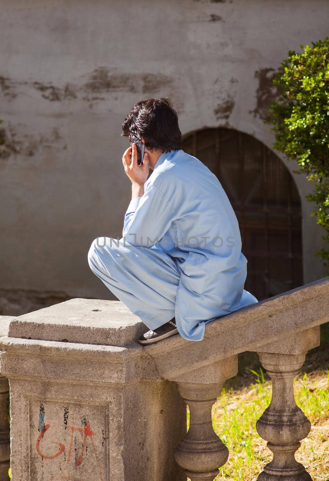 TRIESTE, ITALY - MAY, 05: Afghan boy sitting on balaustrade talking with his phone on May 05, 2016