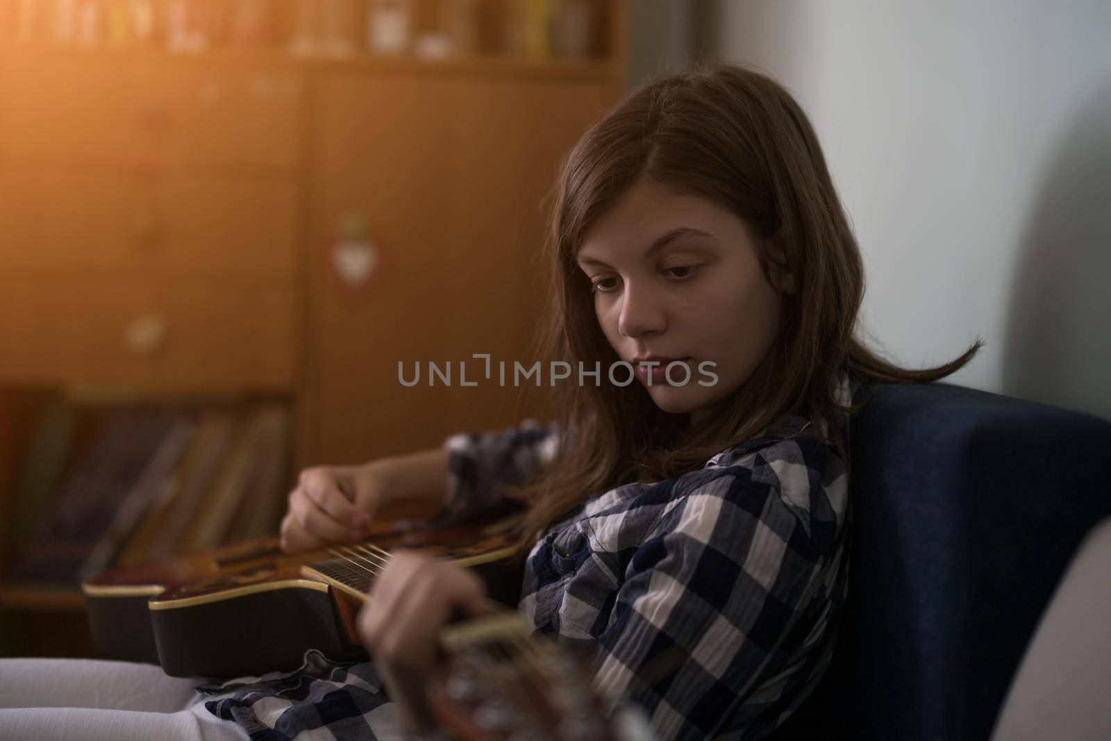 Teenage girl is playing guitar at home.