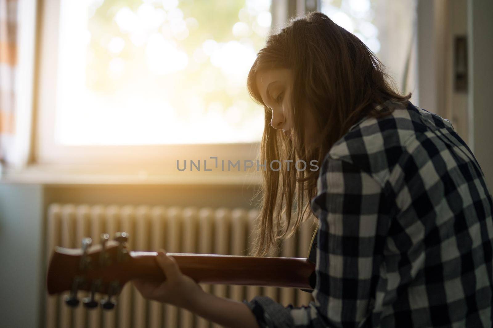 Teenage girl is playing guitar at home.