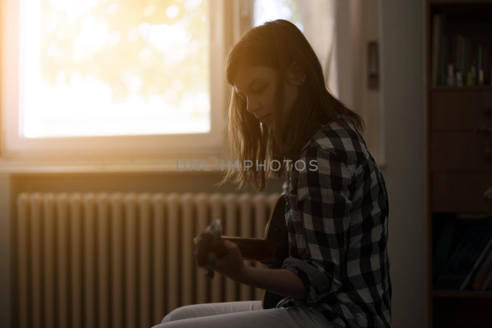 Teenage girl is playing guitar at home.