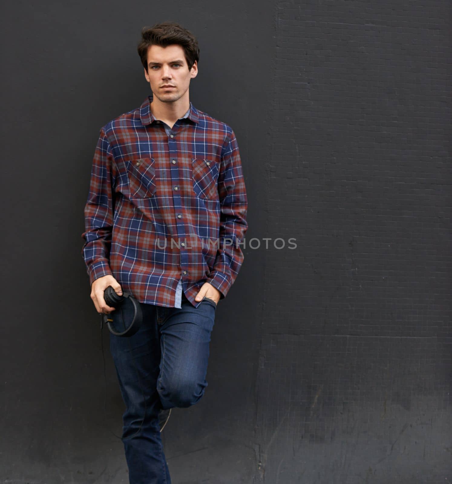 Laid back in plaid. a handsome young man standing outdoors with his earphones