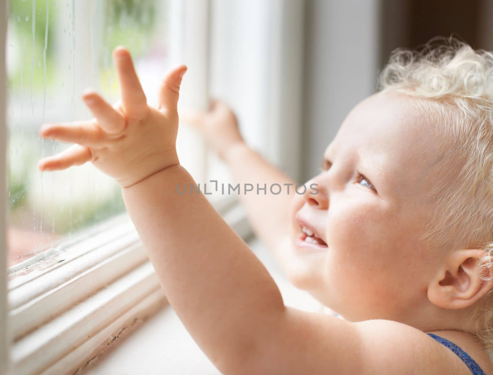 Gazing in wonder at the world. A cute little toddler looking through a window in wonder