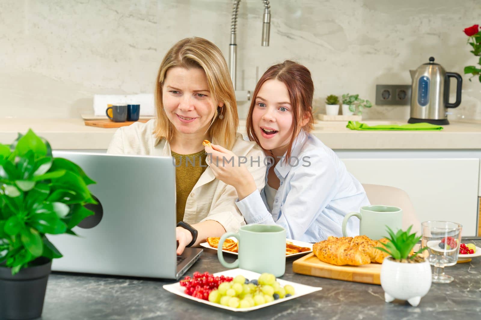 Happy mother and daughter having breakfast in kitchen and using digital devices. Lifestyle by PhotoTime